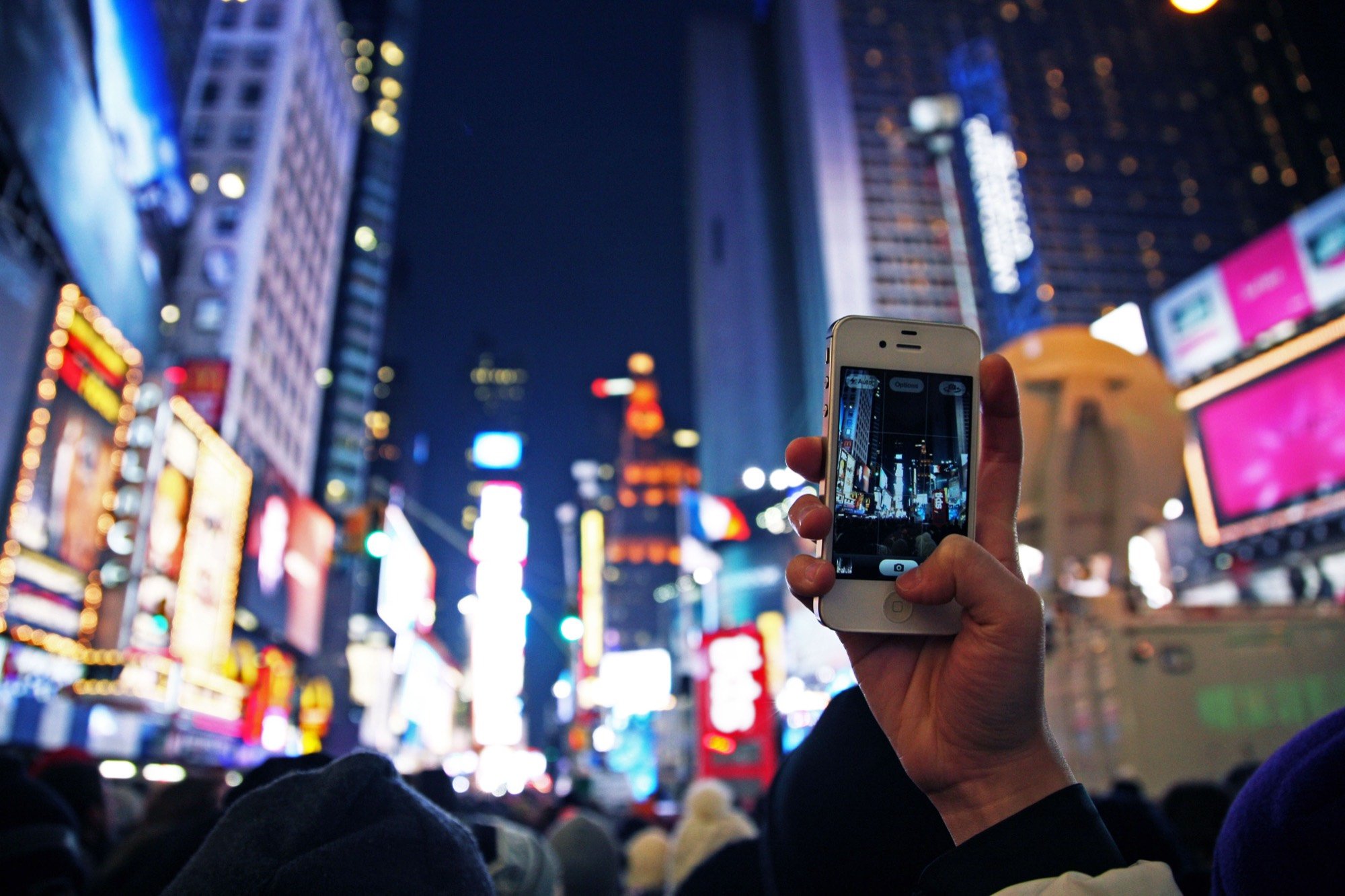 A hand holding a phone up to Times Square at night