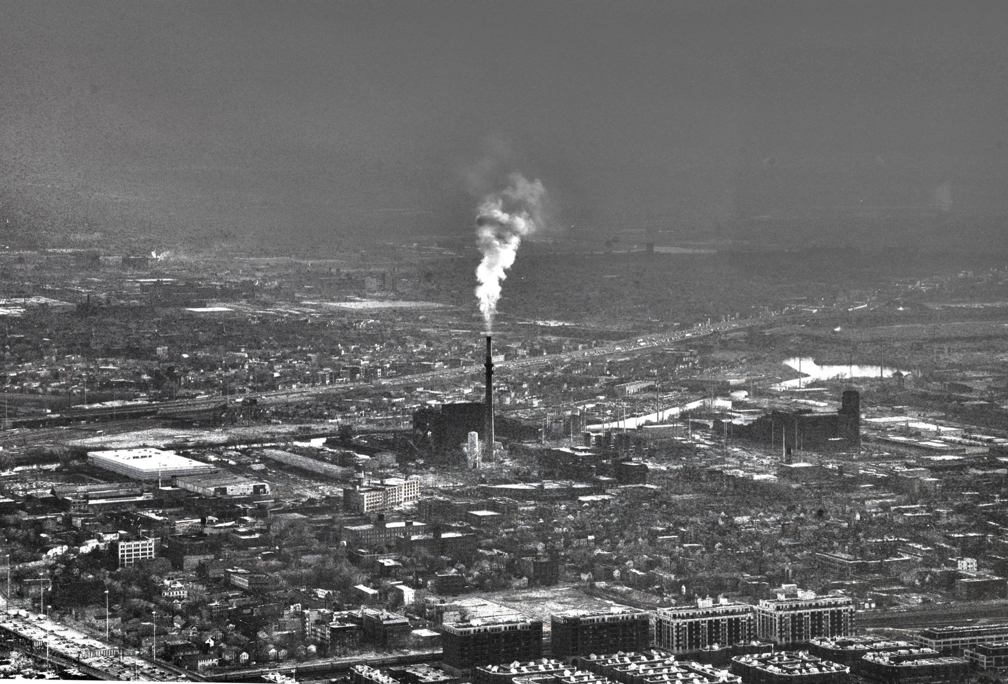 A smoking chimney amid a sprawling city from above