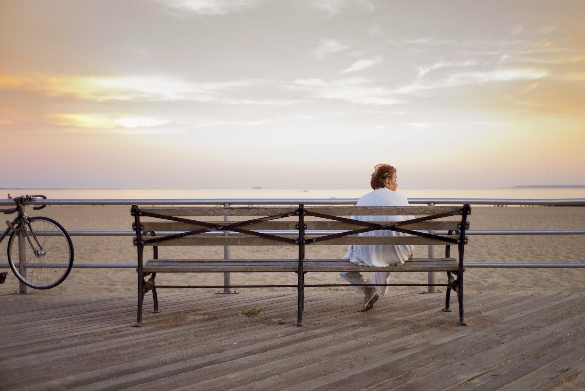 A woman on a boardwalk bench watching the sea at dawn