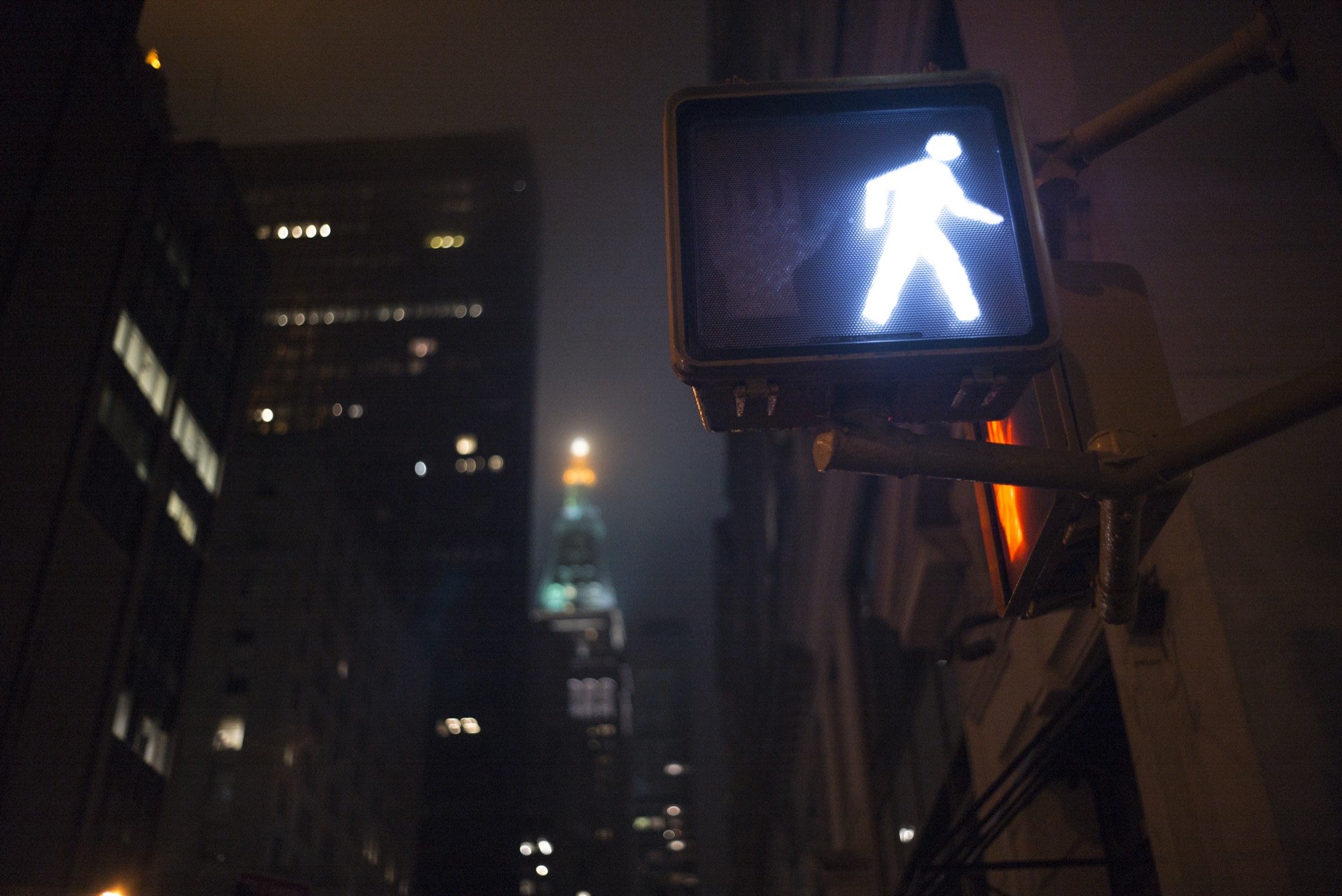 A lit walk signal against a night skyline