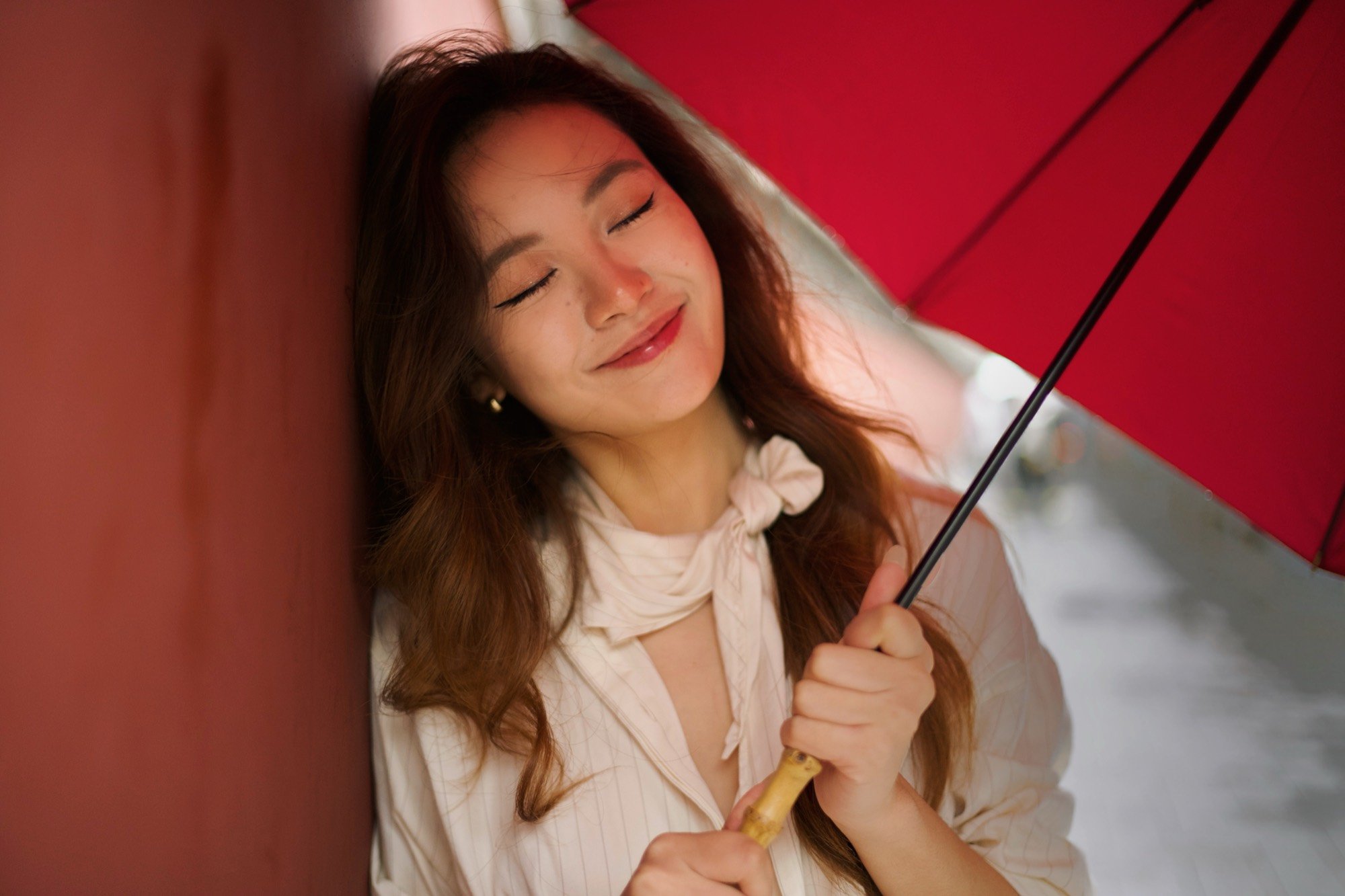 A woman with a red umbrella resting against a red wall