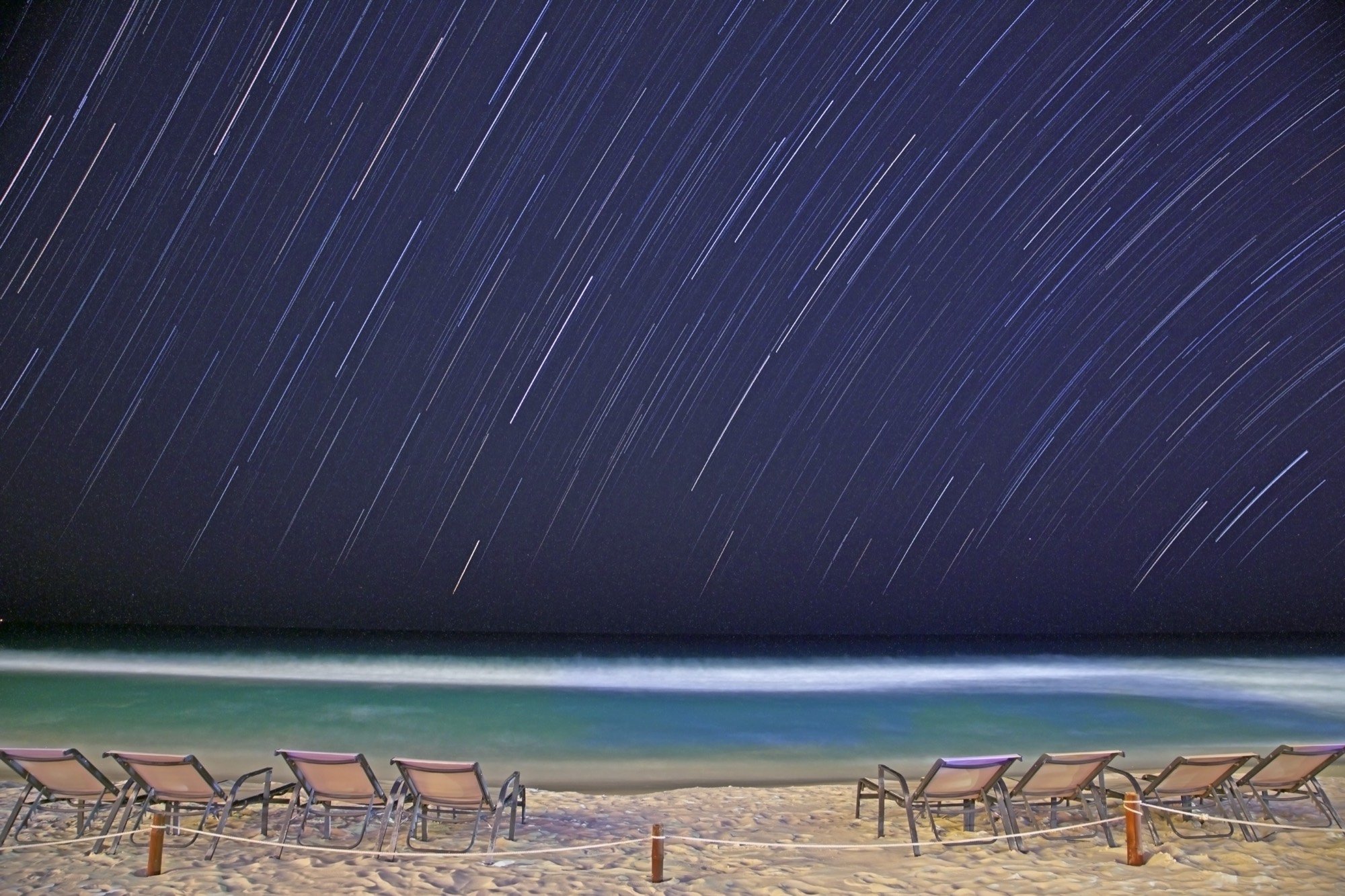 Star trails wheeling over beach loungers at night